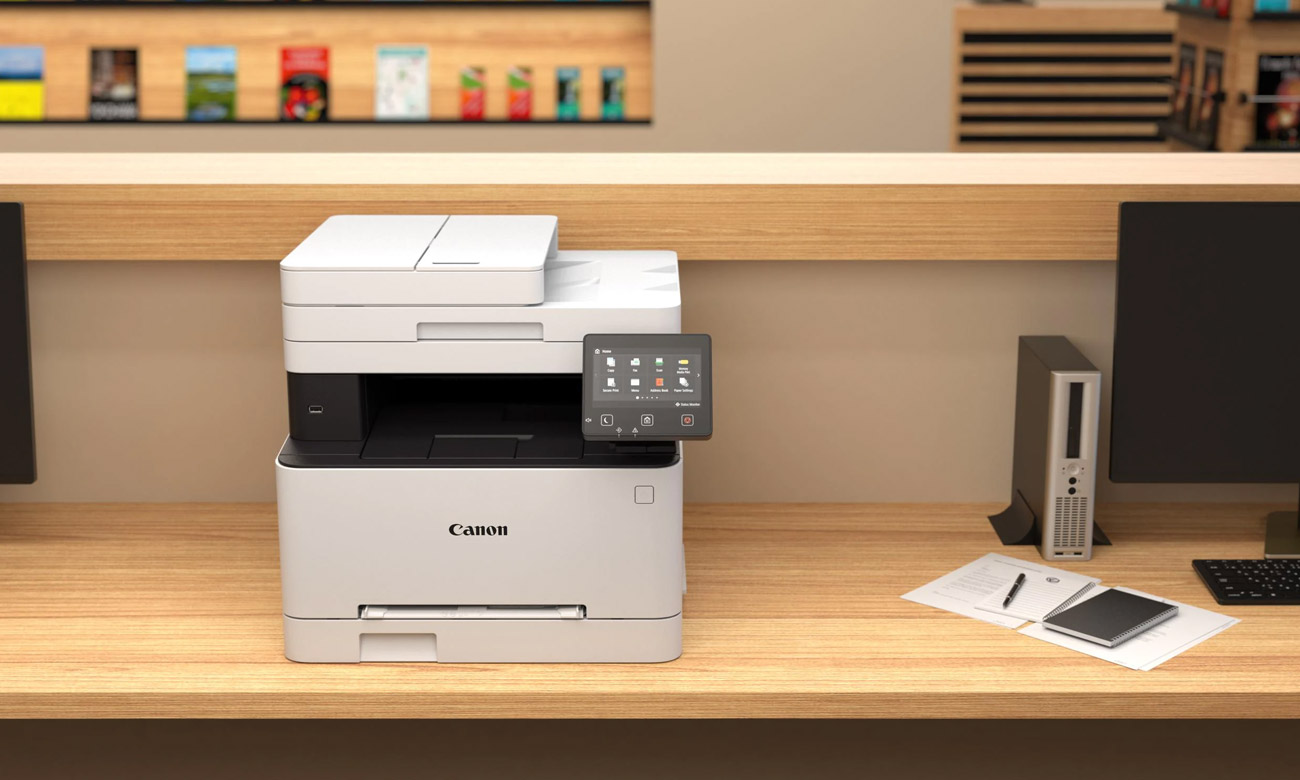 Canon i-SENSYS MF655CDW auf einem Schreibtisch neben einem Monitor