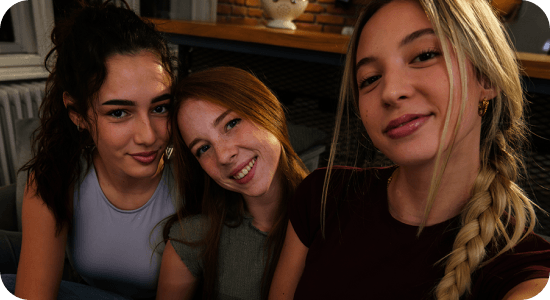 Drei Mädchen auf einem Sofa machen ein Selfie bei schwachem Licht; Nightography des Galaxy A37 5G liefert helle, lebendige Details.